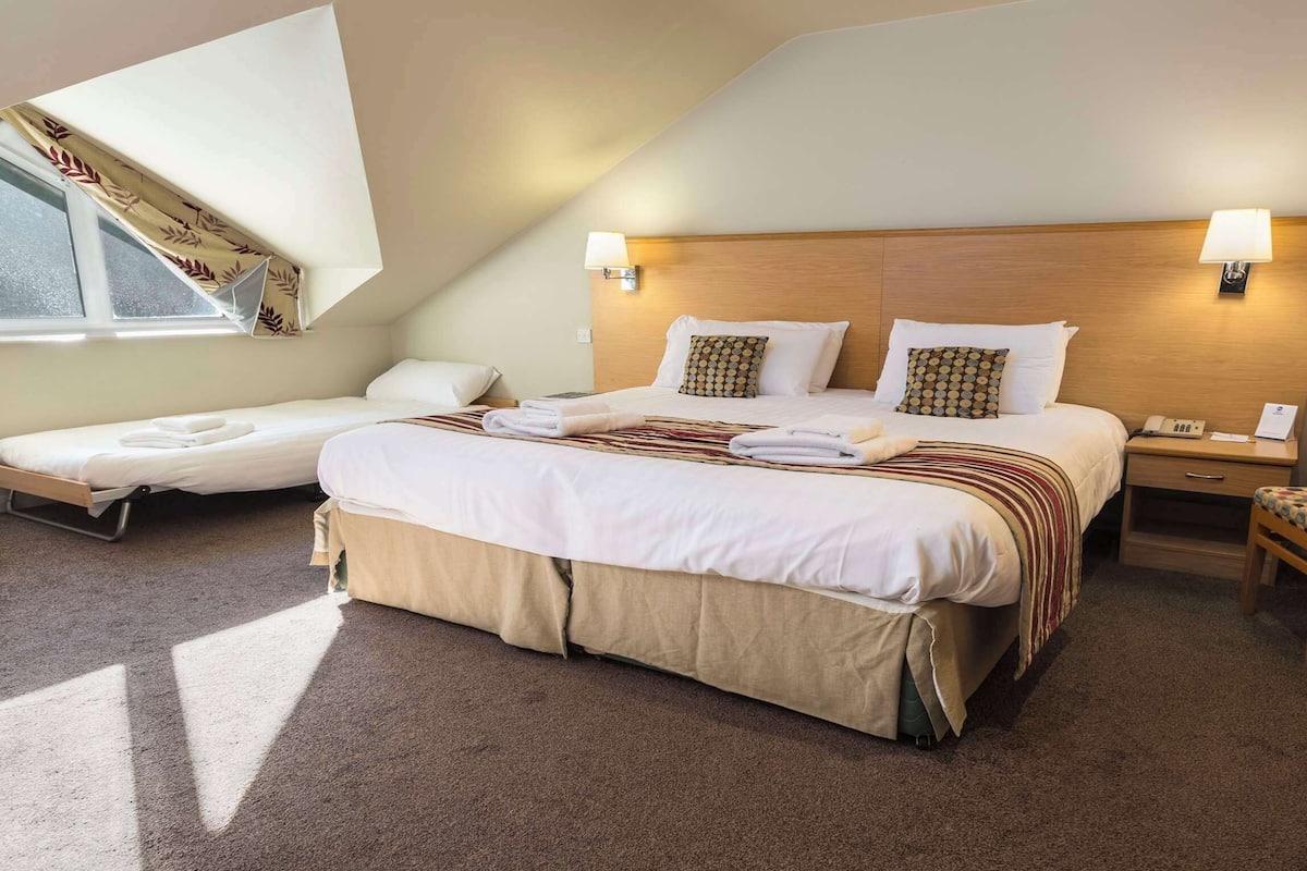 Habitación de hotel con una cama grande, dos mesitas de noche, un escritorio, una silla y una ventana con cortinas.