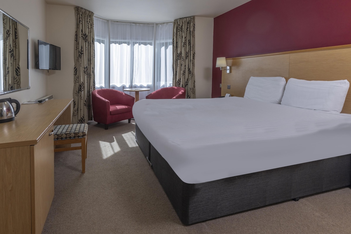 Habitación de hotel con una cama grande, un escritorio con silla, televisión y una ventana con cortinas.