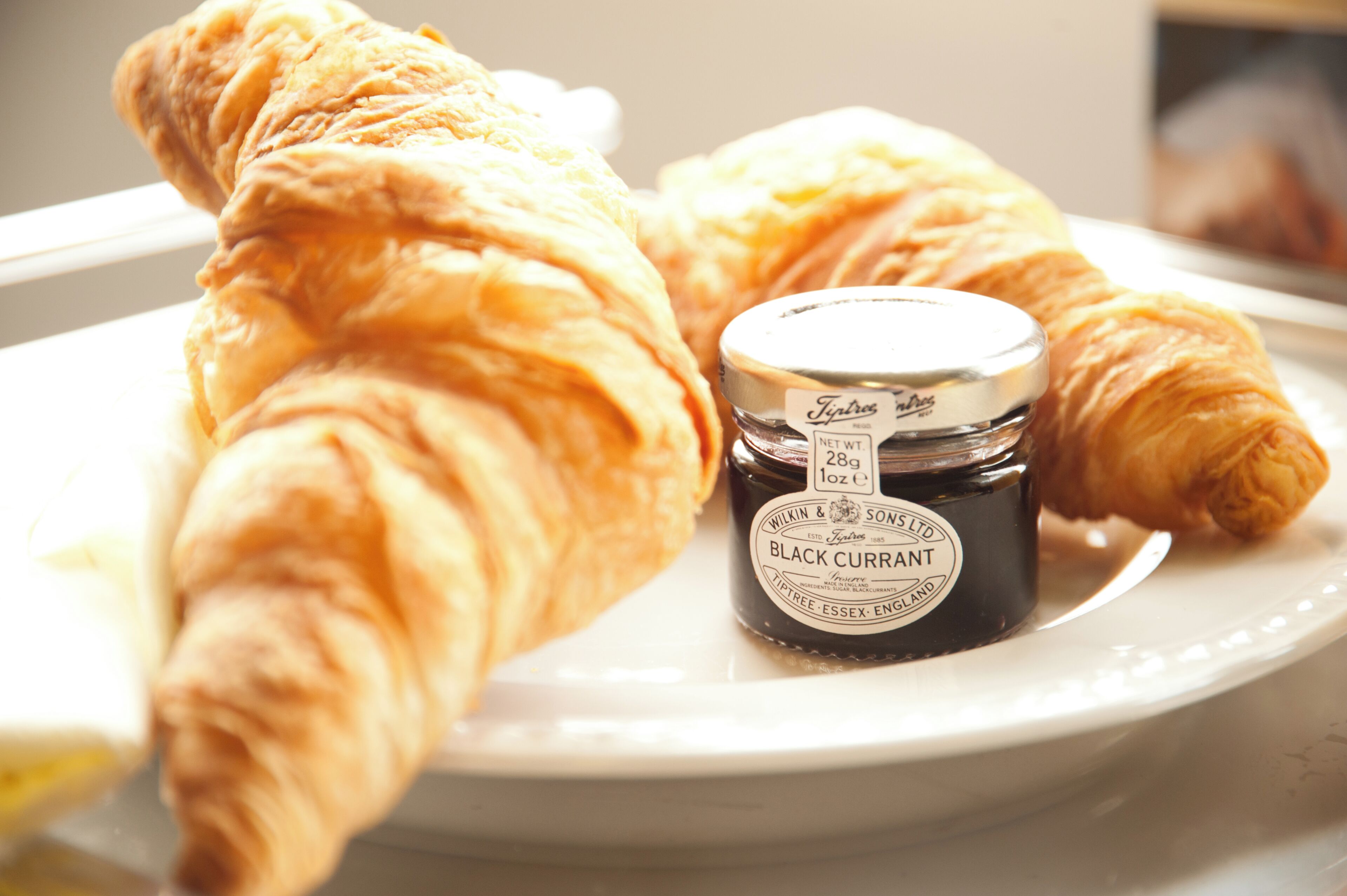 Een bord met twee croissants en een pot vlierbessenjam.