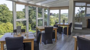 A modern dining area with large windows, wooden tables, and black chairs. - Best Western The Dartmouth Hotel Golf & Spa (Totnes)
