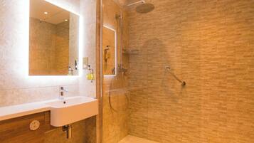 Un baño moderno con ducha de vidrio, un lavabo blanco y un espejo.