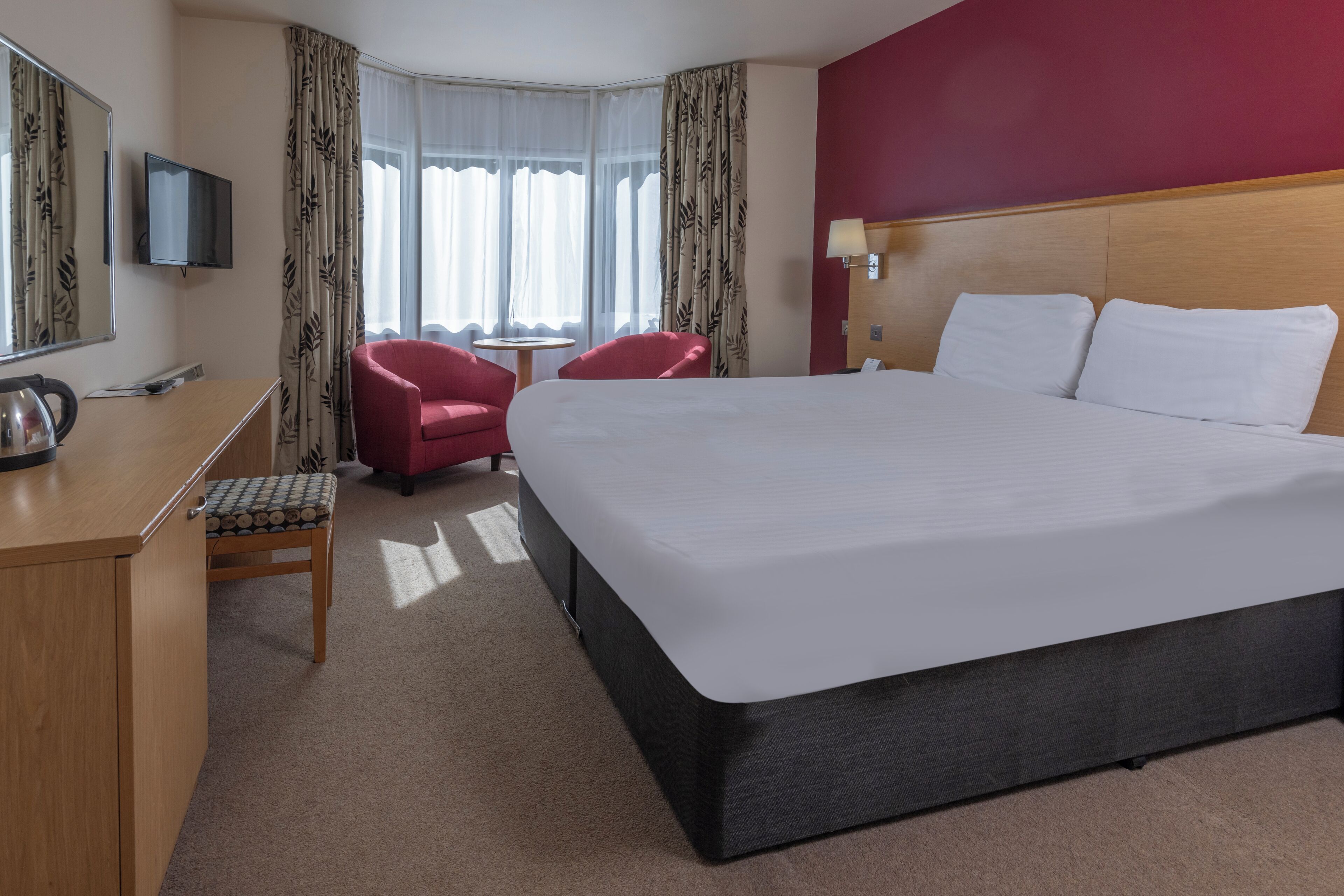 A hotel room with a bed, a desk, a chair, a television, and a window with curtains.