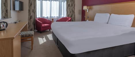 Habitación de hotel con cama, escritorio, silla, televisor y ventana con cortinas.
