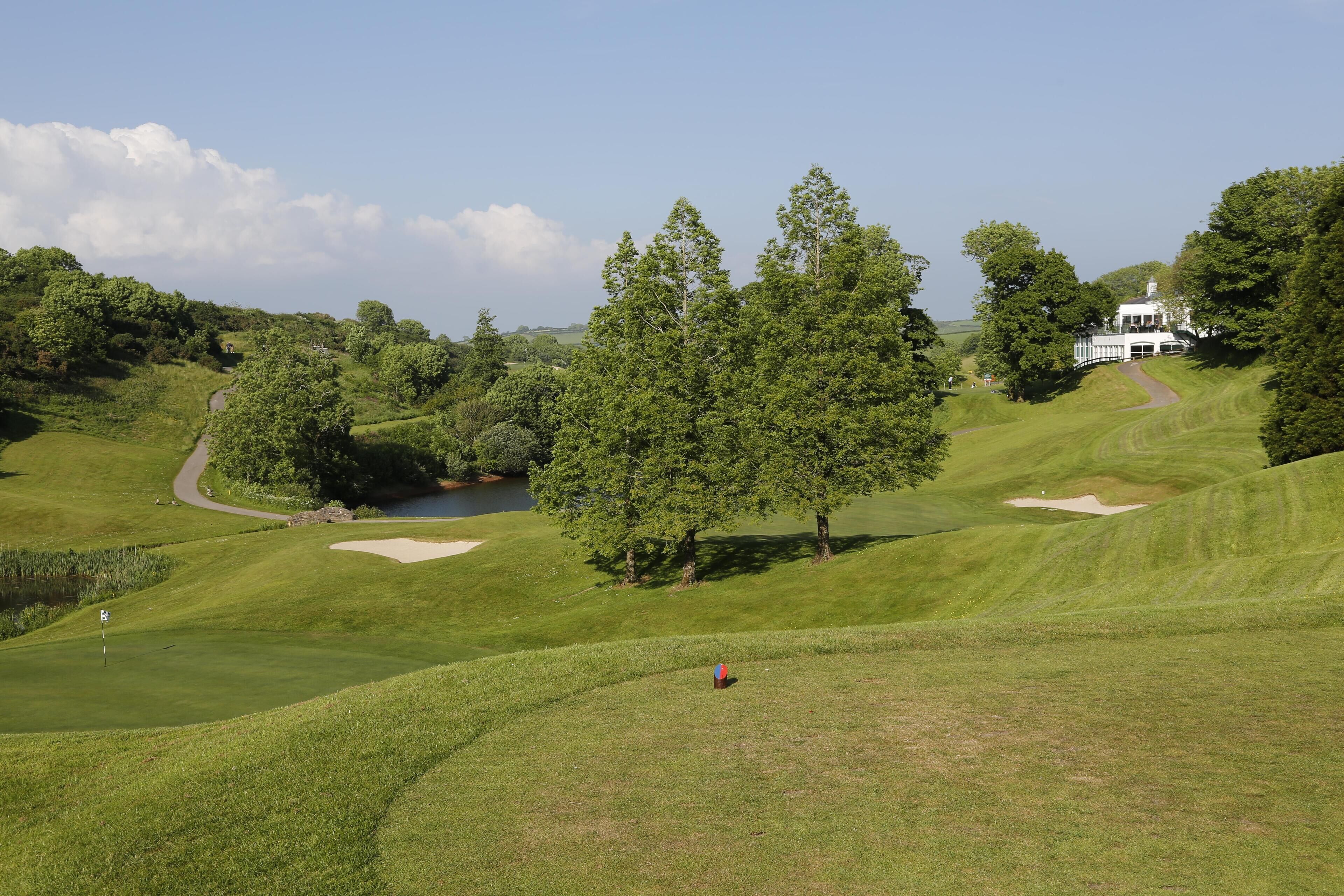 A golf course with a clubhouse, trees, and a pond.