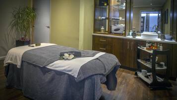 Un dormitorio ordenado con cama, mesita de noche, espejo, planta en maceta y un baño visible a través de una puerta abierta.