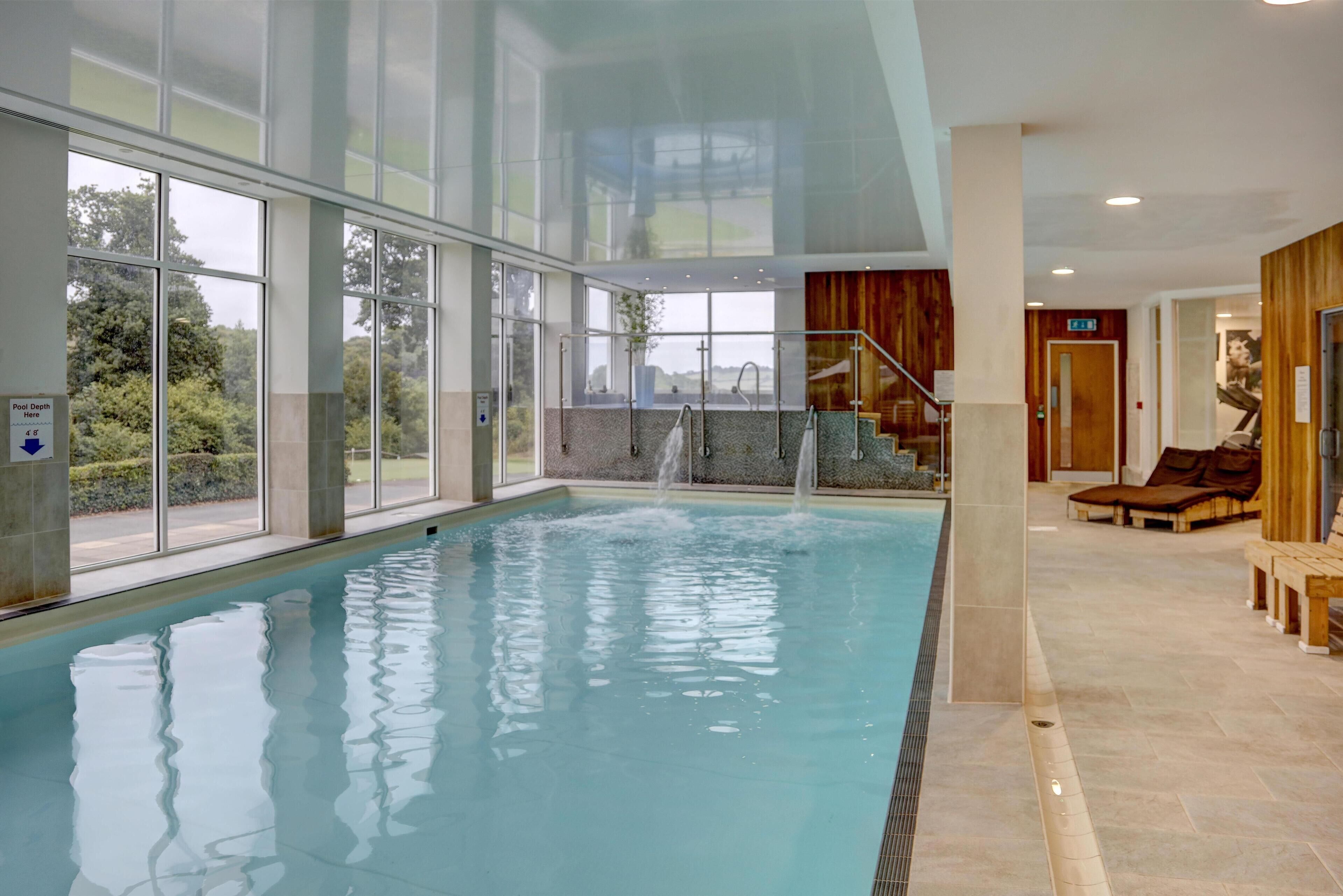 An indoor swimming pool with clear glass walls, a tiled floor, and a view of the outdoors.
