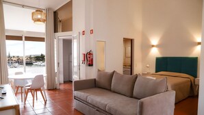 A hotel room with a sofa, a bed, a dining table with chairs, and a view of a marina. - Marina Plaza - Apartments (Loule)