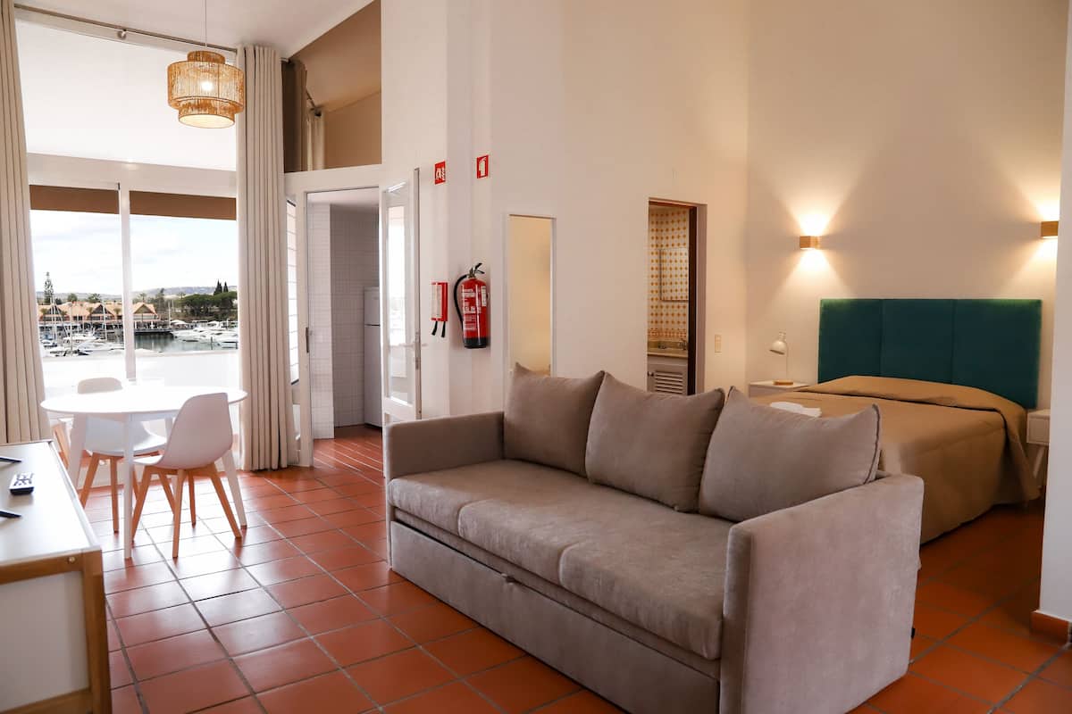 Une chambre d’hôtel avec un canapé, un lit, une table à manger avec des chaises et une vue sur un port de plaisance.