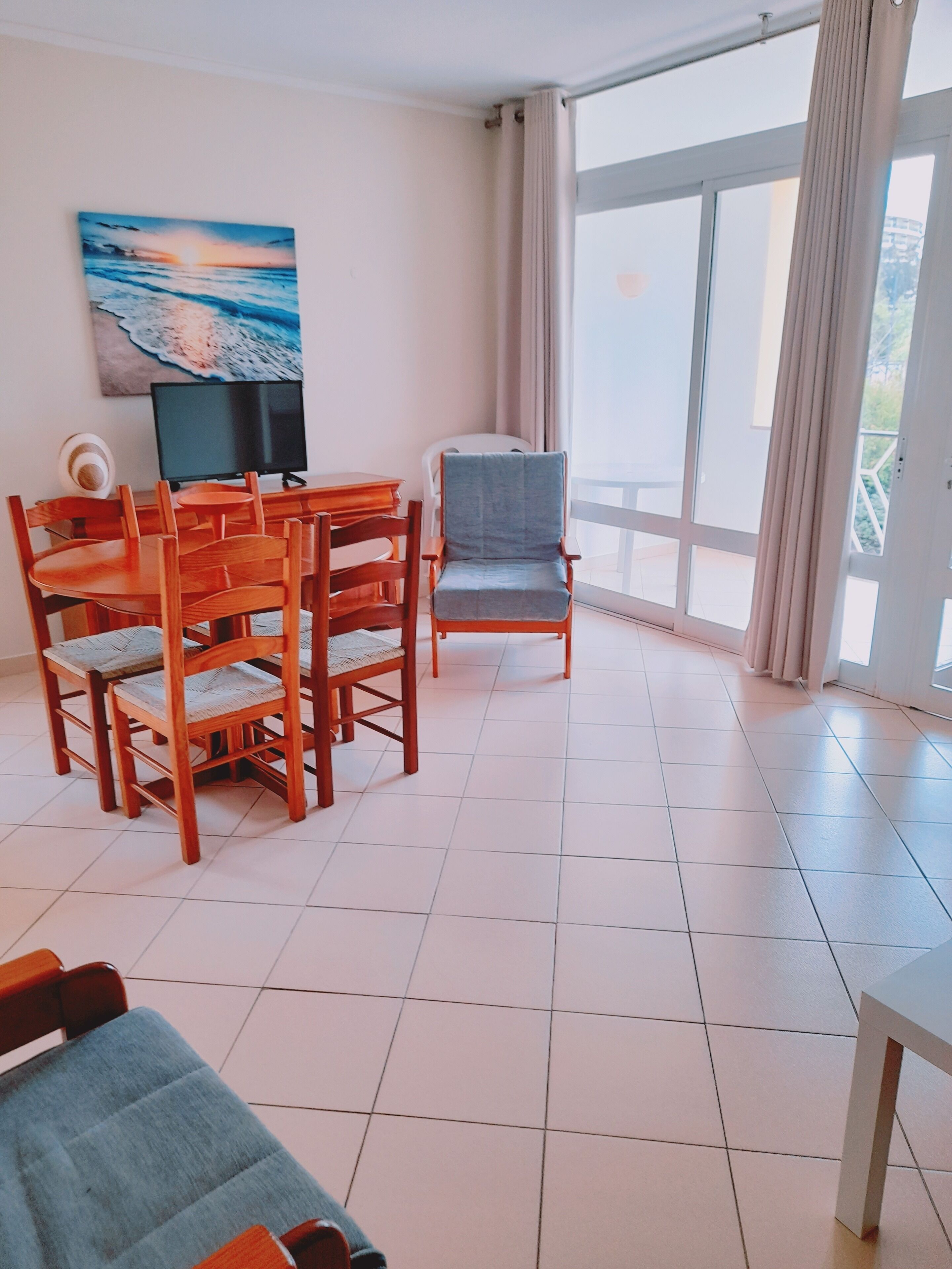 Una habitación amplia con una mesa de comedor y sillas, un televisor y un gran ventanal con cortinas.