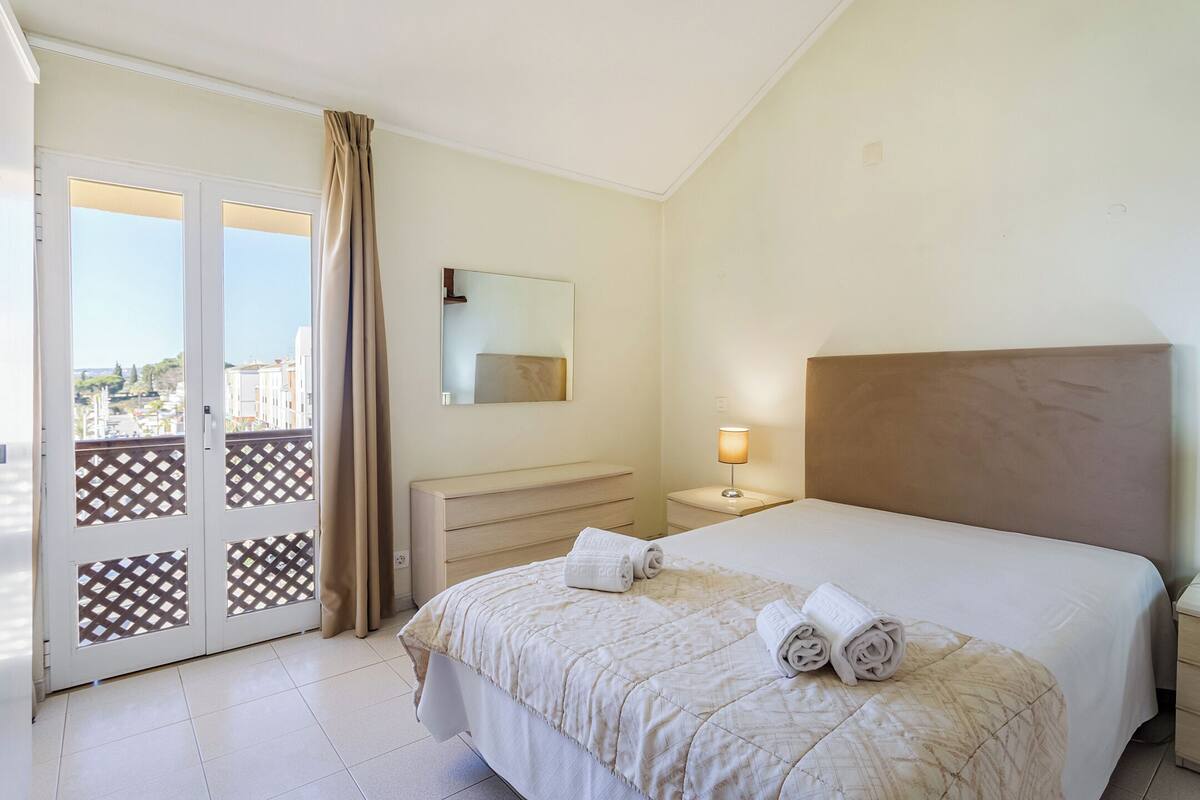 Une chambre d’hôtel avec un lit, une table de chevet, une commode, un miroir et une vue sur l’extérieur.