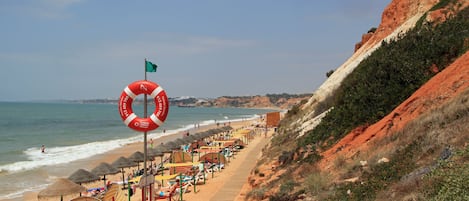 A beach with a lifebuoy, umbrellas, and a wooden walkway.