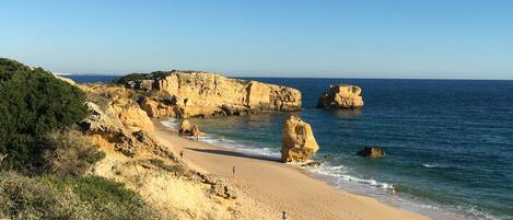 A beach with rocky cliffs, clear blue sky, and calm sea.