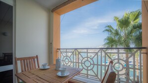 A balcony with a wooden table and chairs, a view of the sea, and a palm tree. - Marina Plaza - Apartments (Loule)