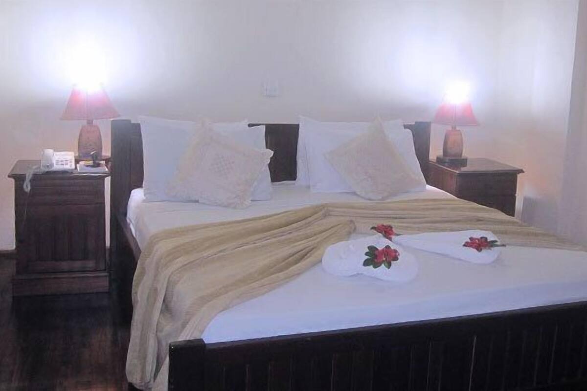 Una cama bien hecha con edredón blanco, dos lámparas de noche y una mesita de noche de madera con un teléfono.