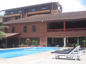 A swimming pool with lounge chairs, a brick building with multiple windows, and a satellite dish. - Coconut Grove Regency Hotel (Accra)
