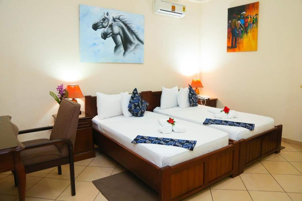 Habitación de hotel con dos camas, una silla, una mesita de noche y dos lámparas de pared.
