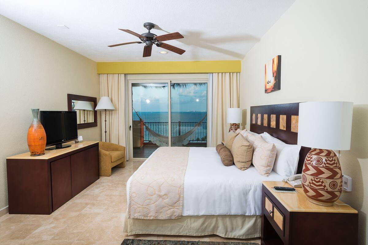 A hotel room with a bed, a television, a desk, a lamp, and a view of the ocean.