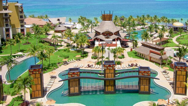 A resort with multiple swimming pools, palm trees, and a central building with a distinctive roof. - Villa del Palmar Cancun Luxury Beach Resort & Spa (Punta Sam)