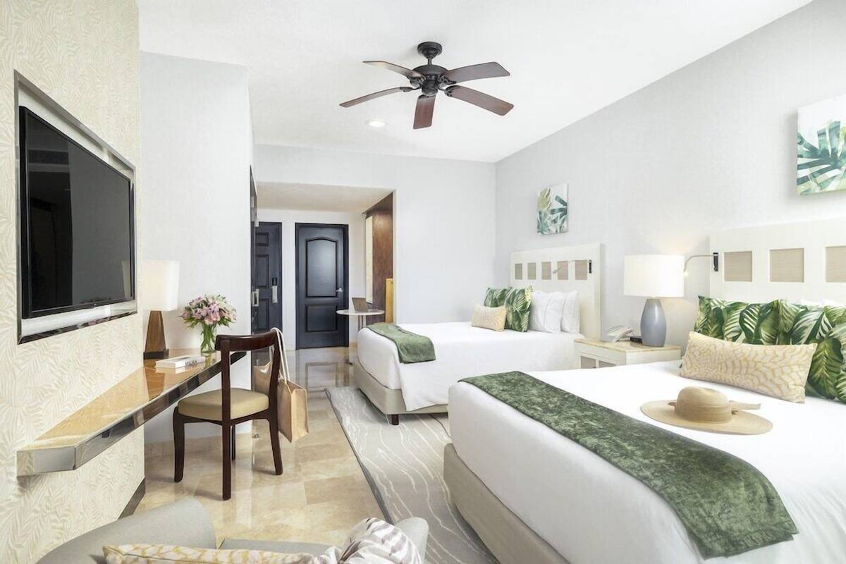 A hotel room with a bed, a desk, a chair, a TV, and a ceiling fan.
