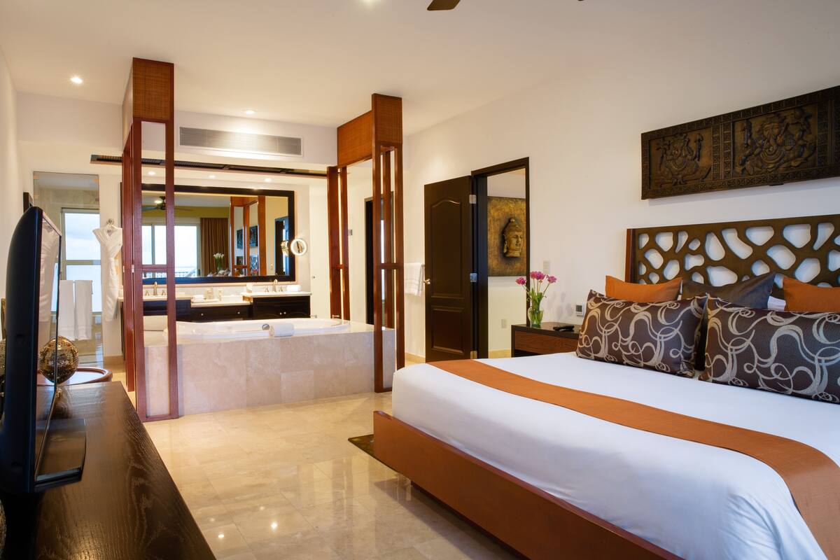 A modern hotel room with a large bed, a separate bathroom with a bathtub, and a television on a wooden table.