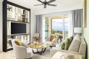 A modern living room with a flat-screen TV, comfortable seating, a balcony with a view, and a ceiling fan.