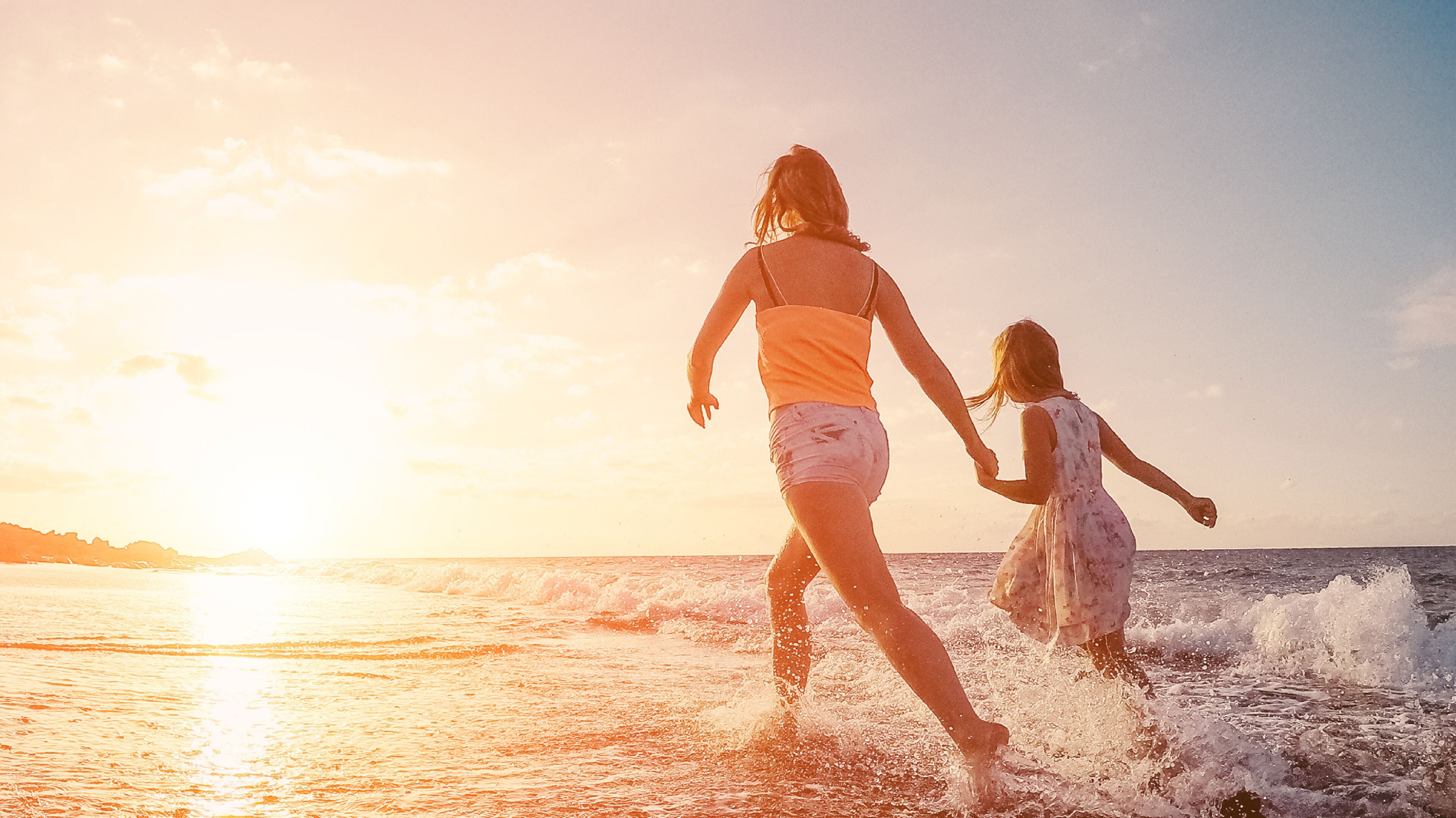 Two people walking on a beach at sunset.