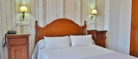 A neatly made bed with white linens, a wooden headboard, and two bedside lamps.