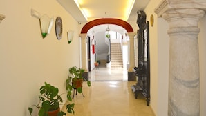 A hallway with a marble floor, potted plants, a staircase, and a column. - Hotel Marisa (Córdoba)