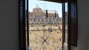A view through a window with ornate ironwork, a balcony, and a building with a dome and arches in the background. - Hotel Marisa (Córdoba)
