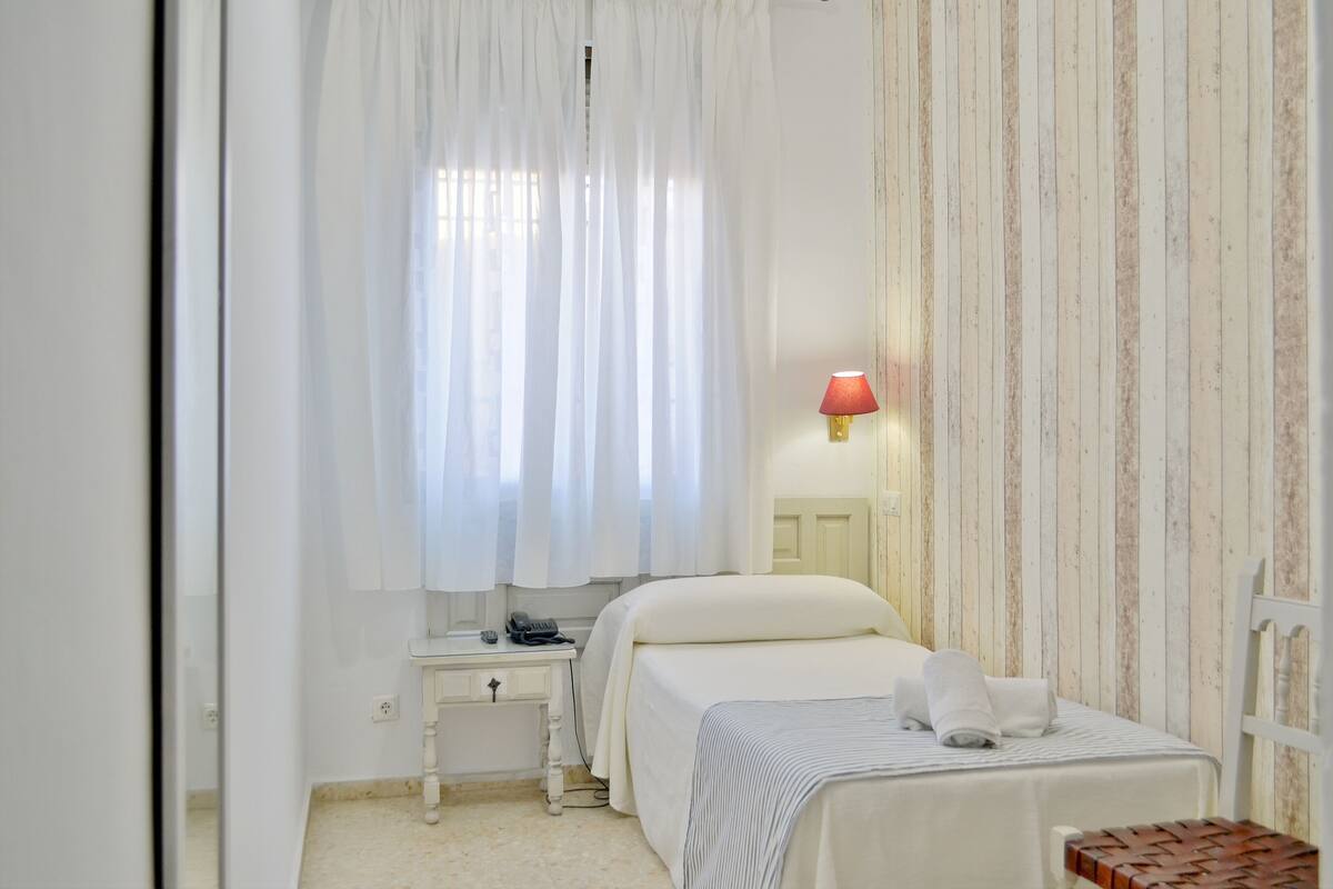 A bedroom with a bed, bedside table, lamp, and curtains.