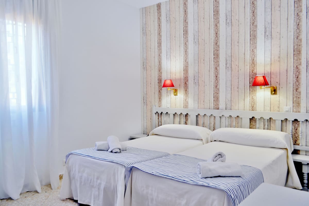 A hotel room with two beds, white bedding, striped blankets, a wooden headboard, and two wall-mounted lamps.