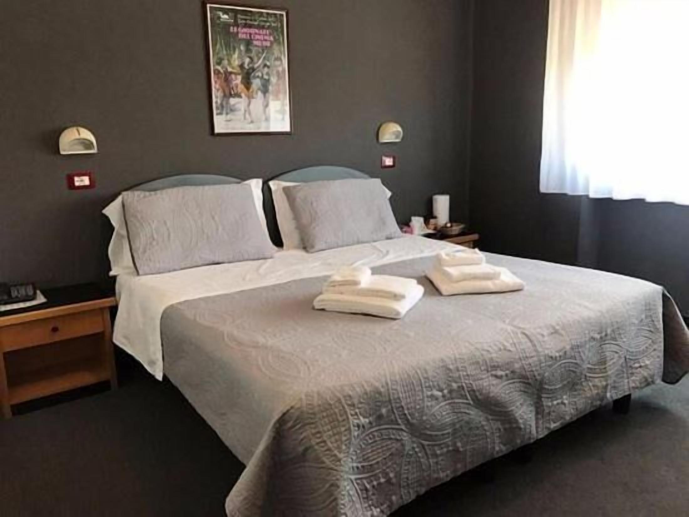 Una cama bien hecha con dos almohadas y dos toallas dobladas. Hay un cartel en la pared sobre la cama.
