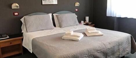 Una cama bien hecha con dos almohadas y dos toallas dobladas. Hay un cartel en la pared sobre la cama.