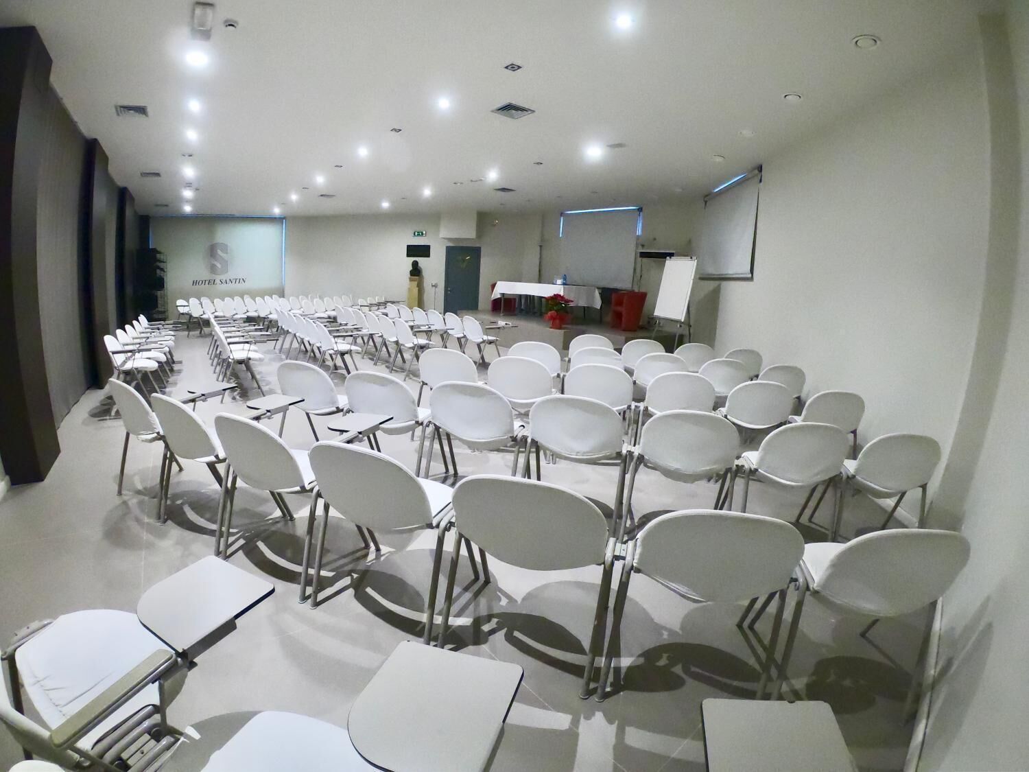 A conference room with rows of white chairs and tables, a podium, and a projection screen.
