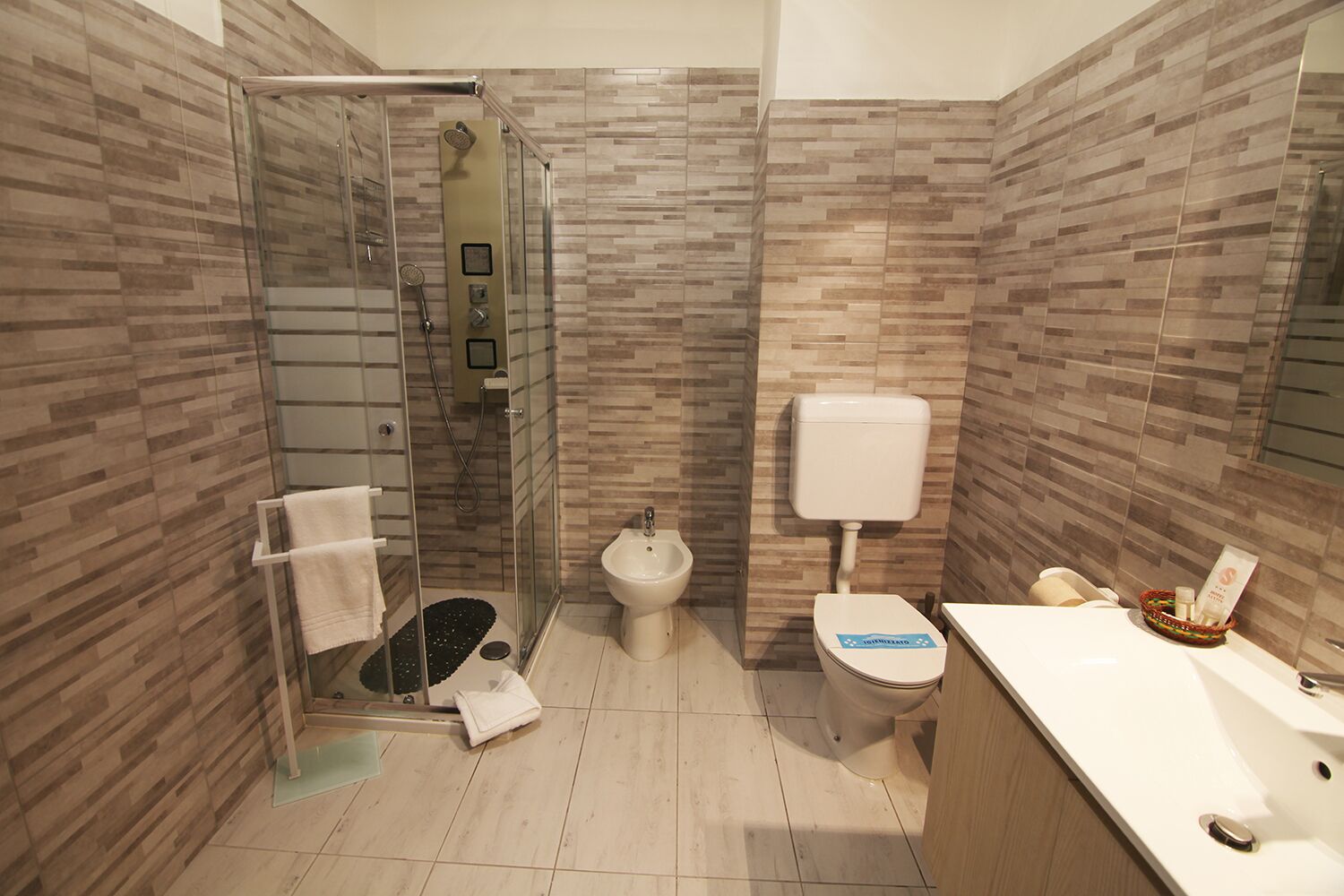 A modern bathroom with a glass shower enclosure, a toilet, and a sink with a towel rack.