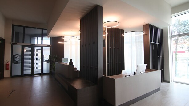 Un área de recepción moderna con un mostrador, ventanas amplias y una escalera que conduce a los pisos superiores.