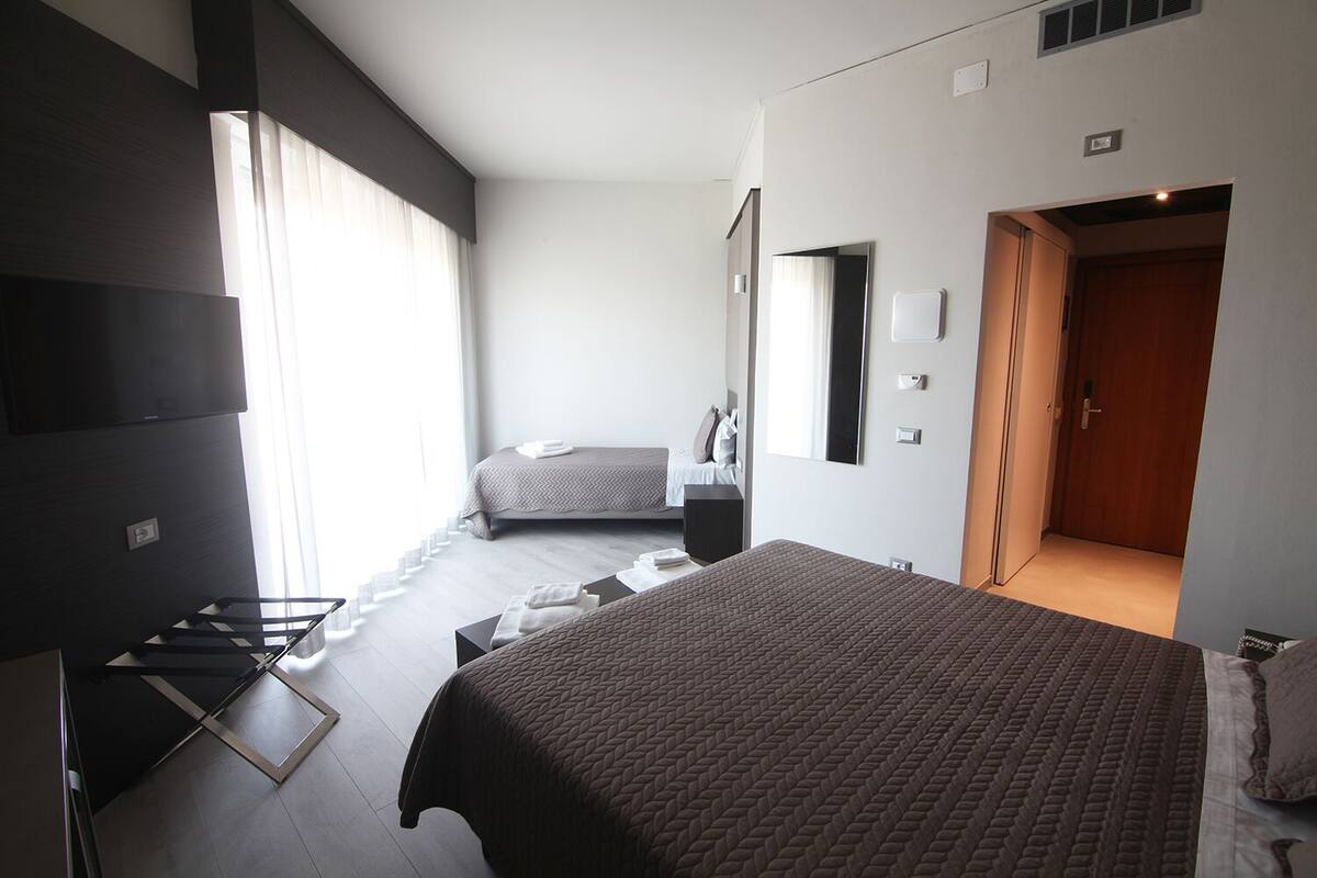 Una habitación de hotel moderna con una cama grande, una cama más pequeña, un televisor y un vestidor.