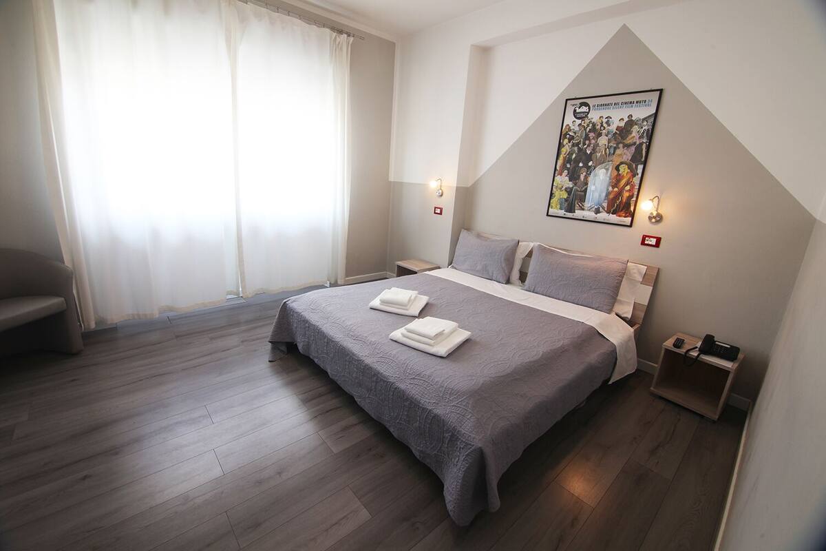 Un dormitorio con cama, mesitas de noche, una ventana con cortinas y un cartel en la pared.