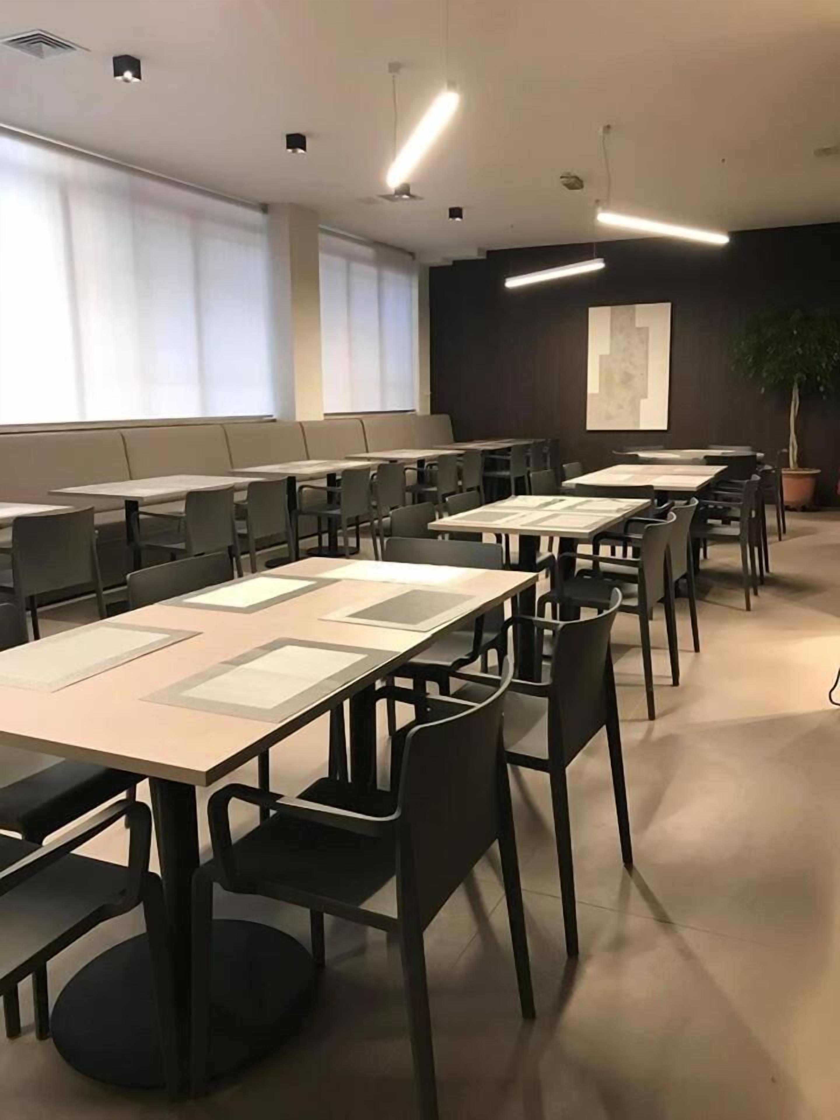 A conference room with long tables and chairs, large windows with blinds, and a potted plant.