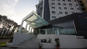 Un hotel moderno con fachada de vidrio, un acceso cubierto y una escalera que lleva a la entrada.