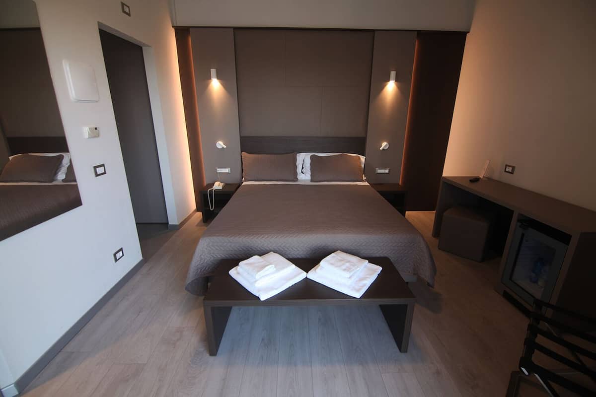Una habitación de hotel moderna con una cama grande, mesitas de noche, televisor y minibar.