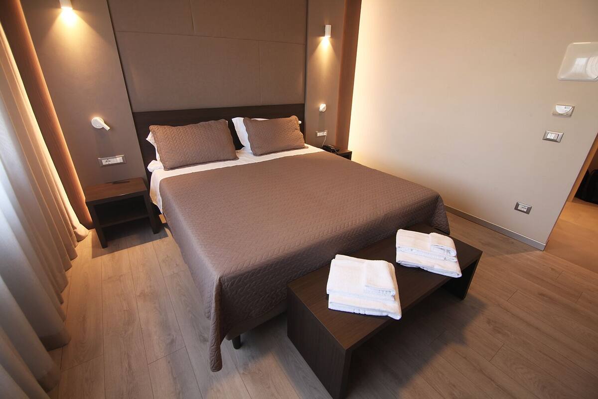 Una habitación de hotel moderna con una cama grande, dos mesitas de noche y suelo de madera.