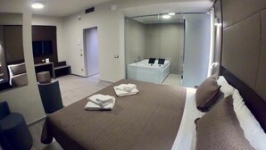 Una habitación de hotel moderna con una cama grande, baño independiente con bañera y zona de estar con televisor.