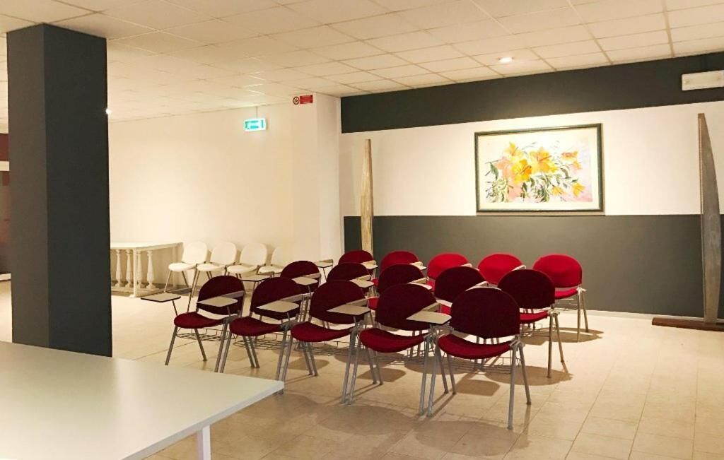 A conference room with red chairs and a white table, a framed painting on the wall, and a black column.