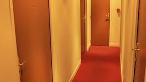 Un couloir d’hôtel avec des portes fermées, une moquette rouge et un panneau indiquant la sortie de secours.