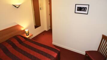 A hotel room with two beds, a nightstand with a lamp, a wooden chair, and a framed picture on the wall.