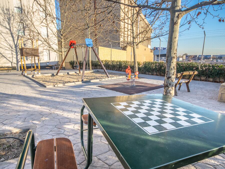 An outdoor chess table with a checkered pattern, surrounded by benches and trees.
