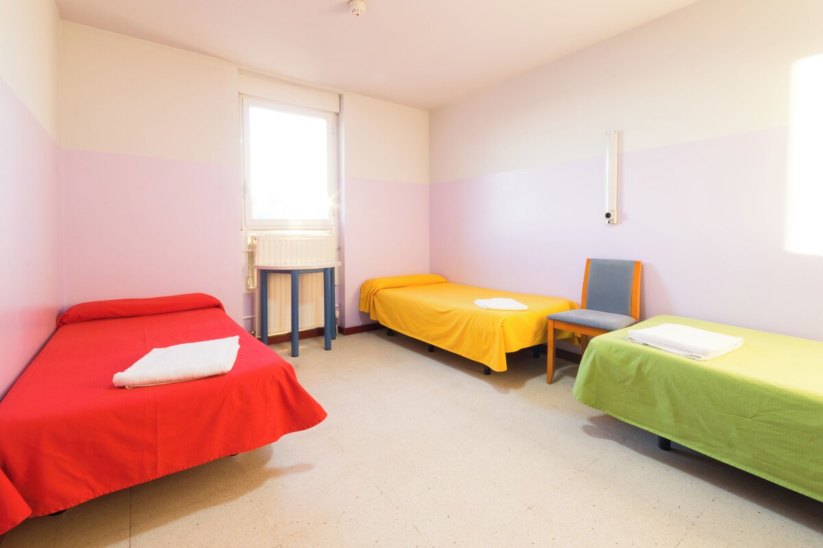 A room with three beds, a window, and a radiator.