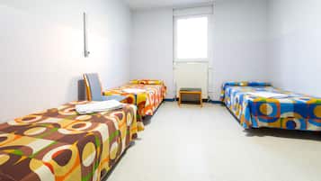 Una habitación con tres camas, cada una con una colcha de colores, un radiador y una ventana.
