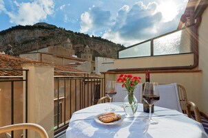 Una mesa con una botella de vino, una copa y un plato de pasteles, con una vista panorámica de montañas al fondo.